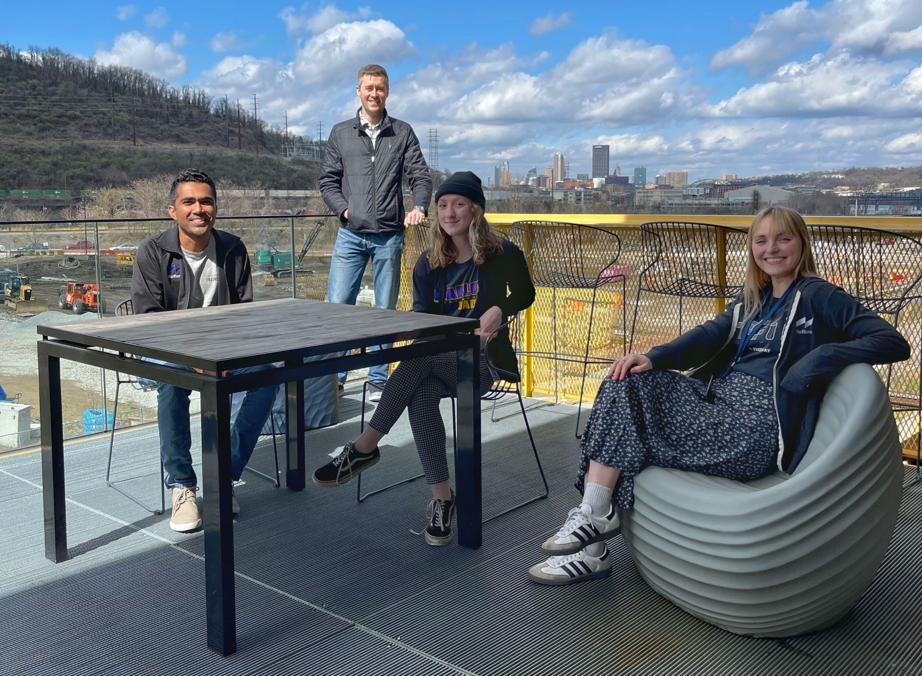 Four Motional employees sit outside on a balcony patio with the Pittsburgh skyline behind them 